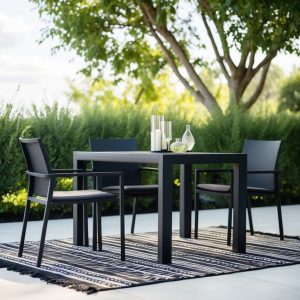 A modern black patio set with clean lines, featuring a sleek table and chairs with minimalist design, set against a backdrop of lush greenery and a stylish outdoor rug