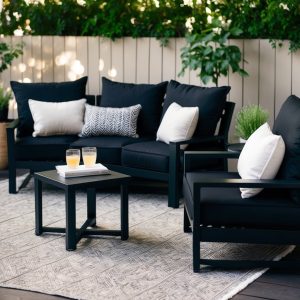 A cozy outdoor space with black patio furniture arranged for maximum comfort, including plush cushions and a small table for drinks or books